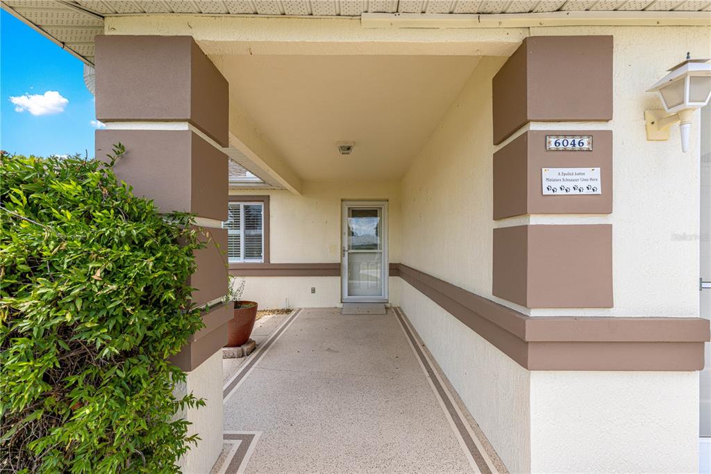 A covered entryway leads to a front door with a house number and decorative sign — 6046 SW 98 LOOP, OCALA, FL