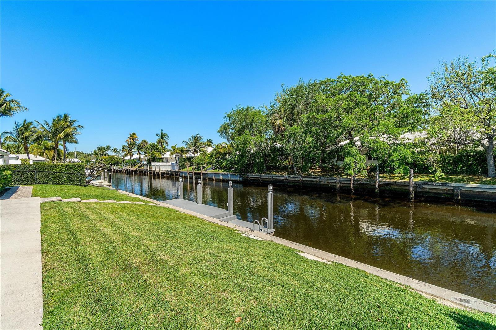 A grassy backyard features a small wooden dock extending into a narrow canal — 976 SW Mulberry Way, Boca Raton FL 33486, BOCA RATON, FL