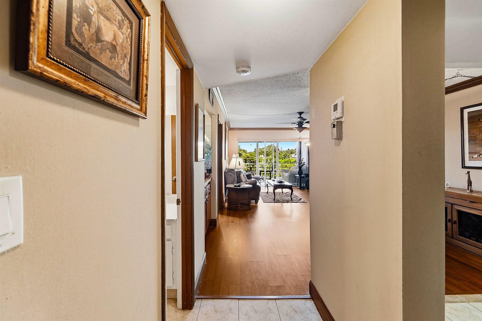 A hallway with light-colored walls leads into a living room with wood-look flooring — 9273 SW 8th Street # 321, Boca Raton FL 33428, BOCA RATON, FL