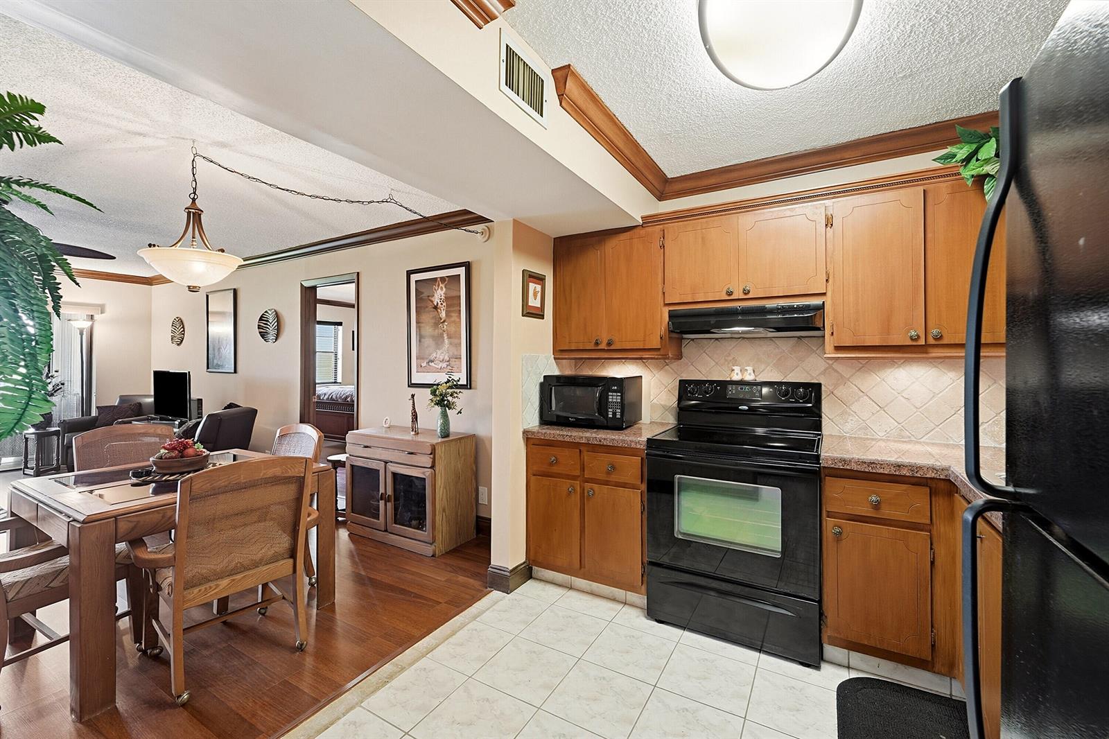A kitchen with wood cabinets and black appliances opens to a dining area with wood floors — 9273 SW 8th Street # 321, Boca Raton FL 33428, BOCA RATON, FL