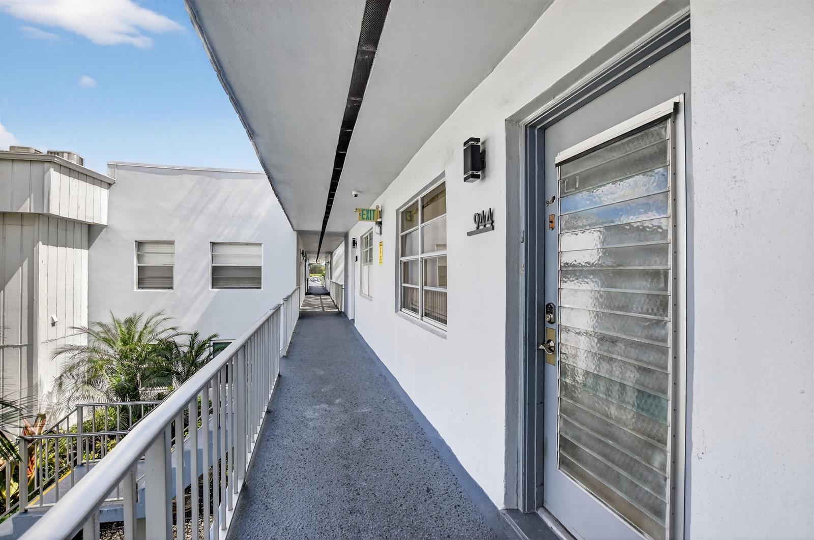 An outdoor apartment walkway features a white building exterior, a numbered door, and metal railings — 944 Normandy Trail # 944, Delray Beach FL 33484, DELRAY BEACH, FL