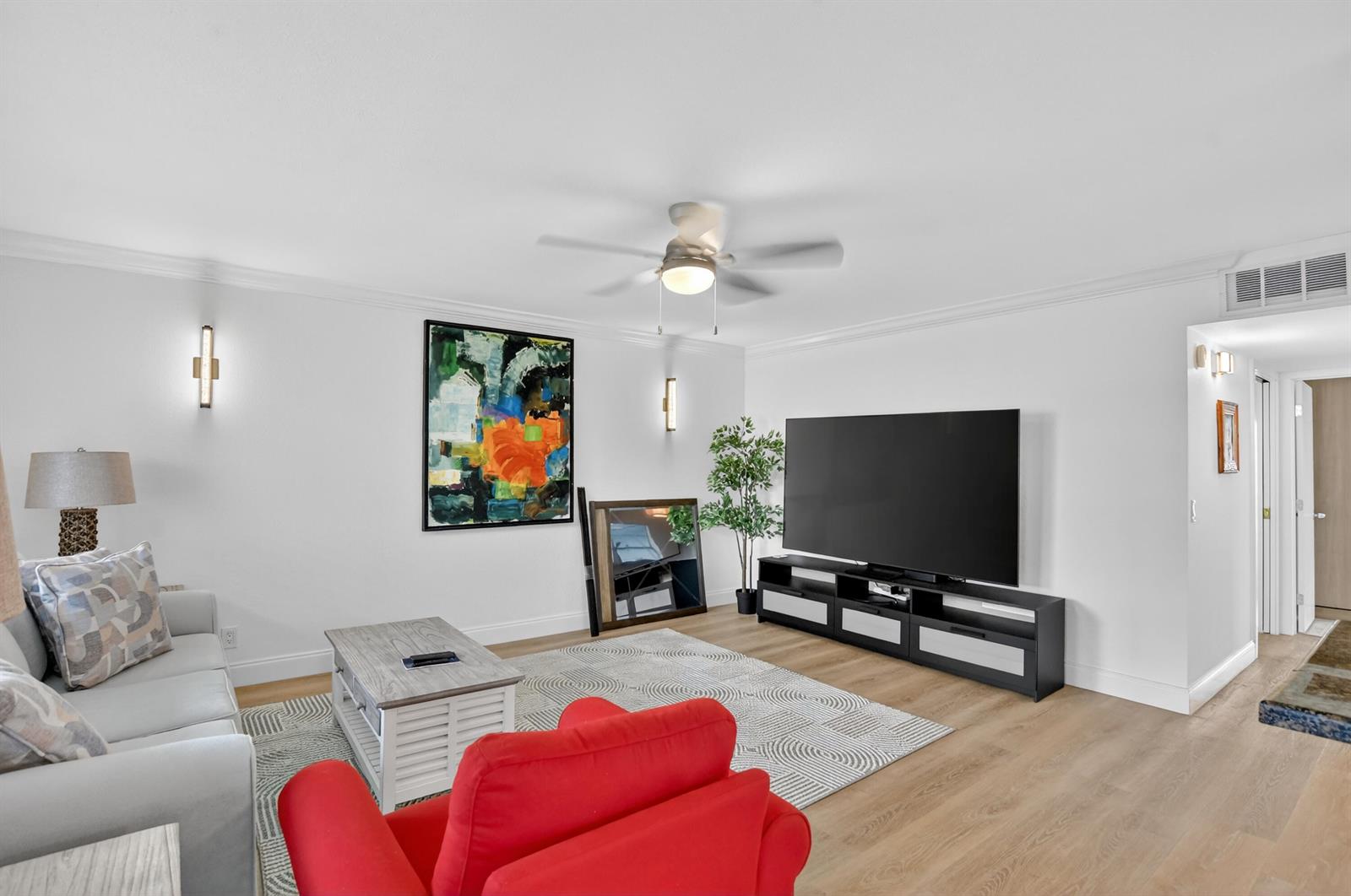 A living room features a large television, a red armchair, a sofa, and modern decor — 944 Normandy Trail # 944, Delray Beach FL 33484, DELRAY BEACH, FL