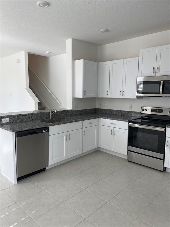 A kitchen features white cabinets, granite countertops, stainless steel appliances, and light-colored tile flooring — 32077 POWDERPUFF MIMOSA, SAN ANTONIO, FL