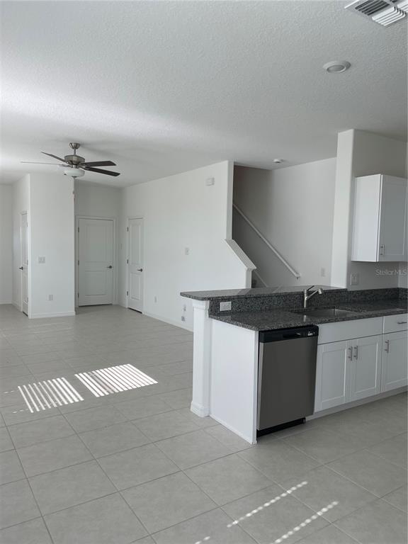 A kitchen with white cabinets and granite countertops opens to a living area with tile — 32077 POWDERPUFF MIMOSA, SAN ANTONIO, FL
