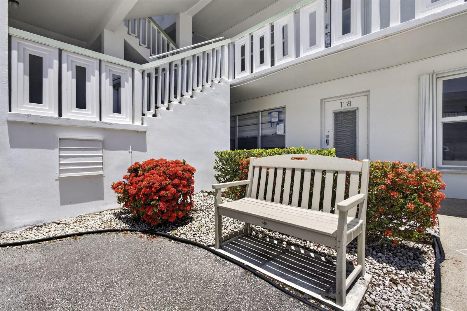 A light-colored wooden bench sits on a gravel bed in front of a white building — 307 Wellington C, West Palm Beach FL 33417, WEST PALM BEACH, FL