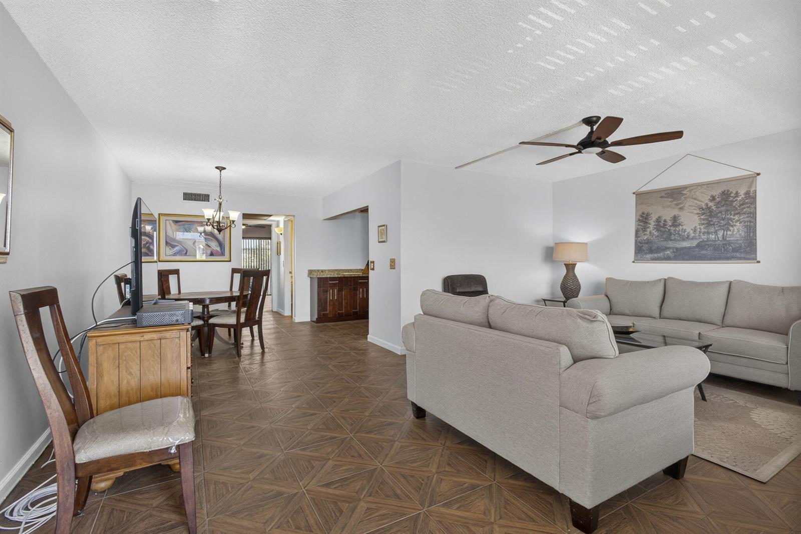 An open-concept living and dining area features tile flooring, neutral furniture, and a ceiling fan — 307 Wellington C, West Palm Beach FL 33417, WEST PALM BEACH, FL