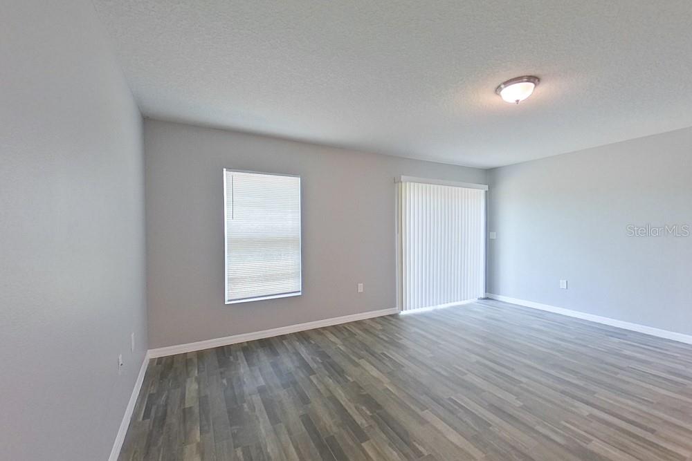 An empty room features gray walls, wood-look flooring, a window with blinds, and sliding doors — 2907 W CAMILO DRIVE, CITRUS SPRINGS, FL