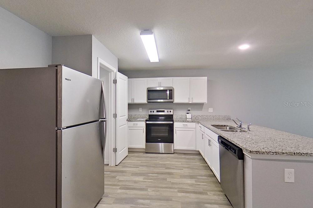 A kitchen features white cabinets, stainless steel appliances, granite countertops, and light wood-look flooring — 2907 W CAMILO DRIVE, CITRUS SPRINGS, FL