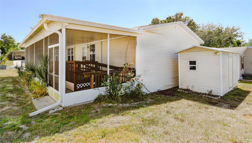A white mobile home exterior features a screened-in porch with a wooden deck and ramp — 11921 SALINA WAY, LEESBURG, FL