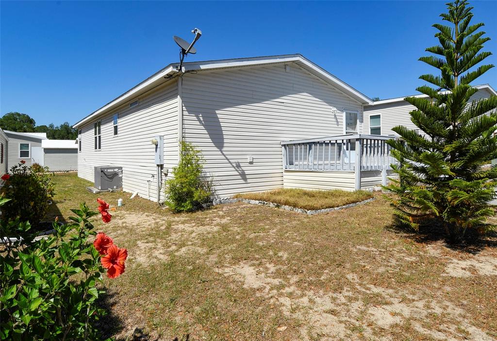 The exterior of a light-colored mobile home features a small wooden deck and landscaping — 11921 SALINA WAY, LEESBURG, FL