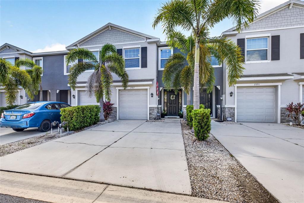 A two-story townhouse exterior features a concrete driveway, a garage, and palm trees — 2387 MIDNIGHT PEARL DRIVE, SARASOTA, FL