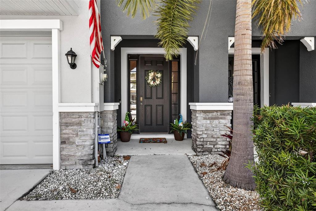 The exterior of a home features a dark front door, stone accents, and a palm tree — 2387 MIDNIGHT PEARL DRIVE, SARASOTA, FL