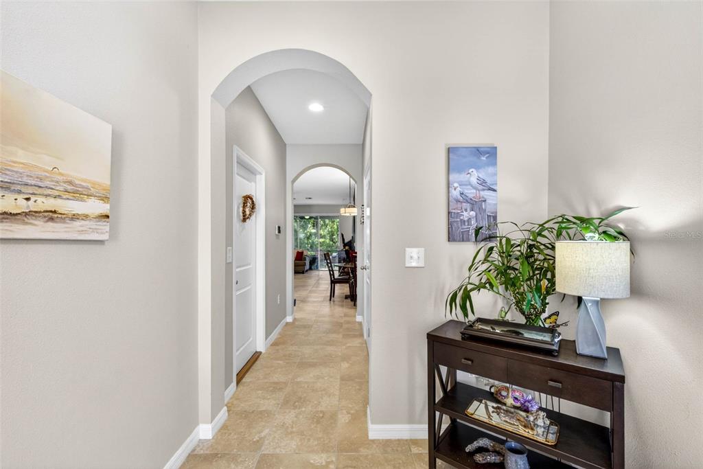 A tiled hallway features arched entryways leading to a living area with a console table — 2387 MIDNIGHT PEARL DRIVE, SARASOTA, FL