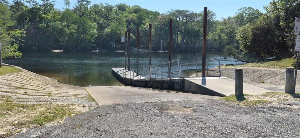 A concrete boat ramp leads into a river with a floating dock and metal pilings — lot 12 NW 70 CIRCLE, CHIEFLAND, FL