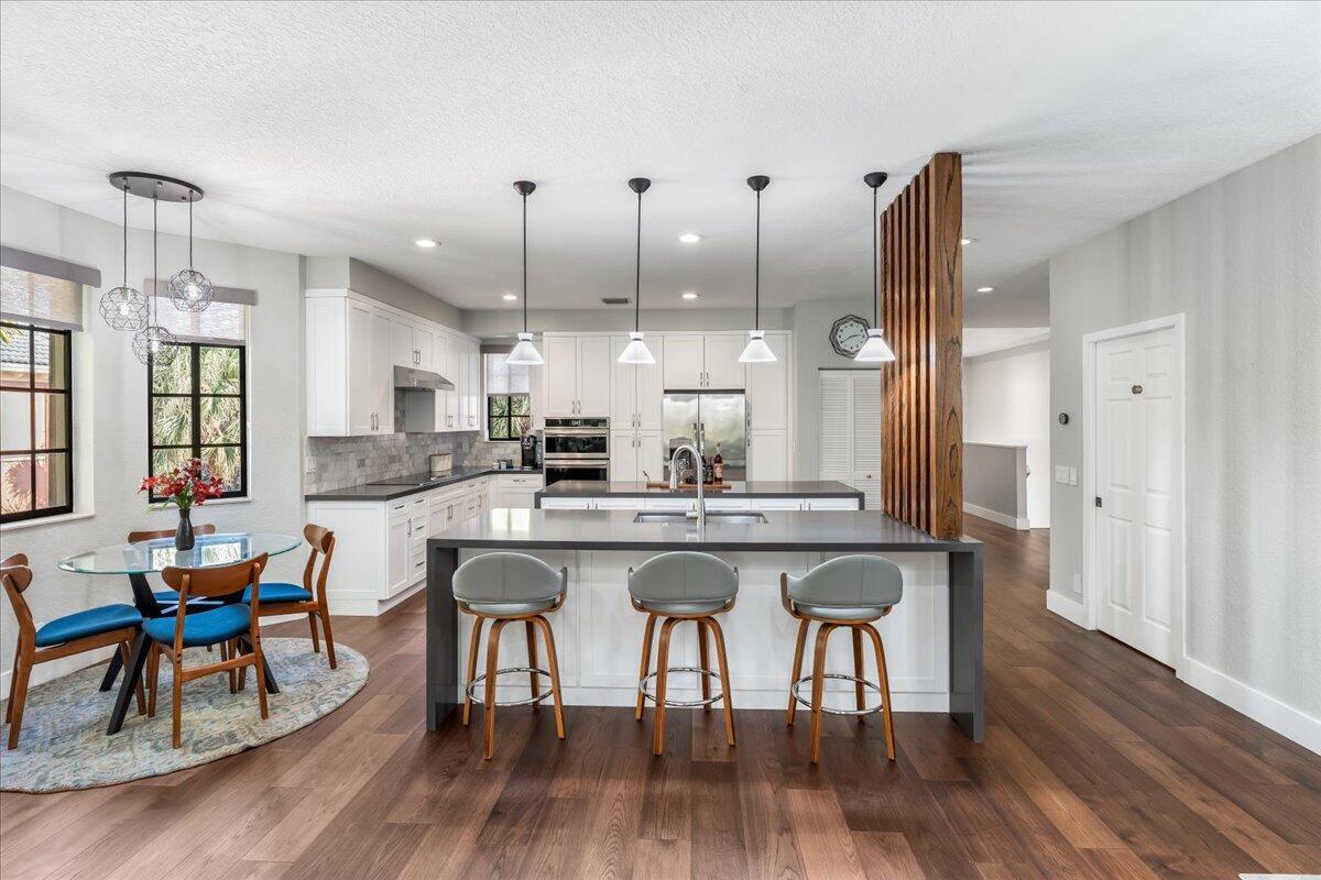 A modern kitchen features white cabinetry, a large gray island with bar seating, and wood flooring — 2802 Kinsington Circle # 4, Weston FL 33332, WESTON, FL