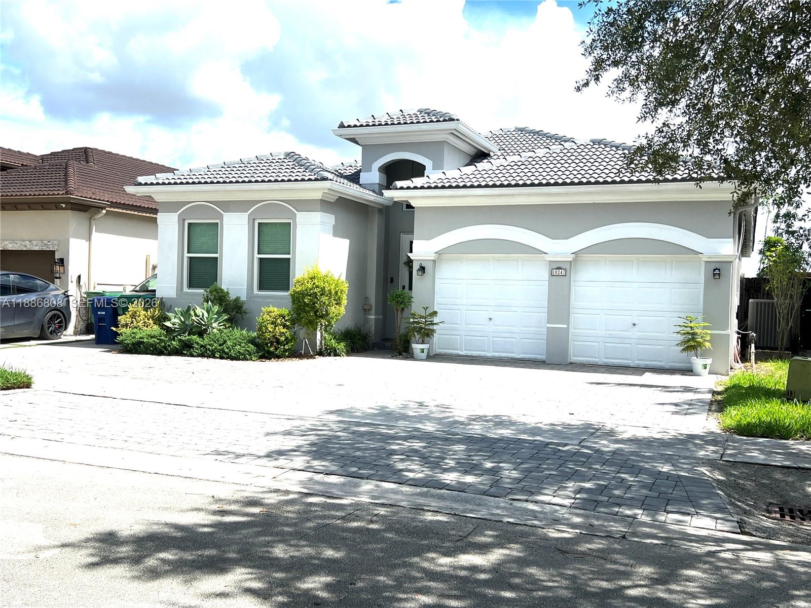 A gray single-story house features a two-car garage, arched window trim, and a paved driveway — 18247 NW 88th Pl, Hialeah FL 33018, HIALEAH, FL