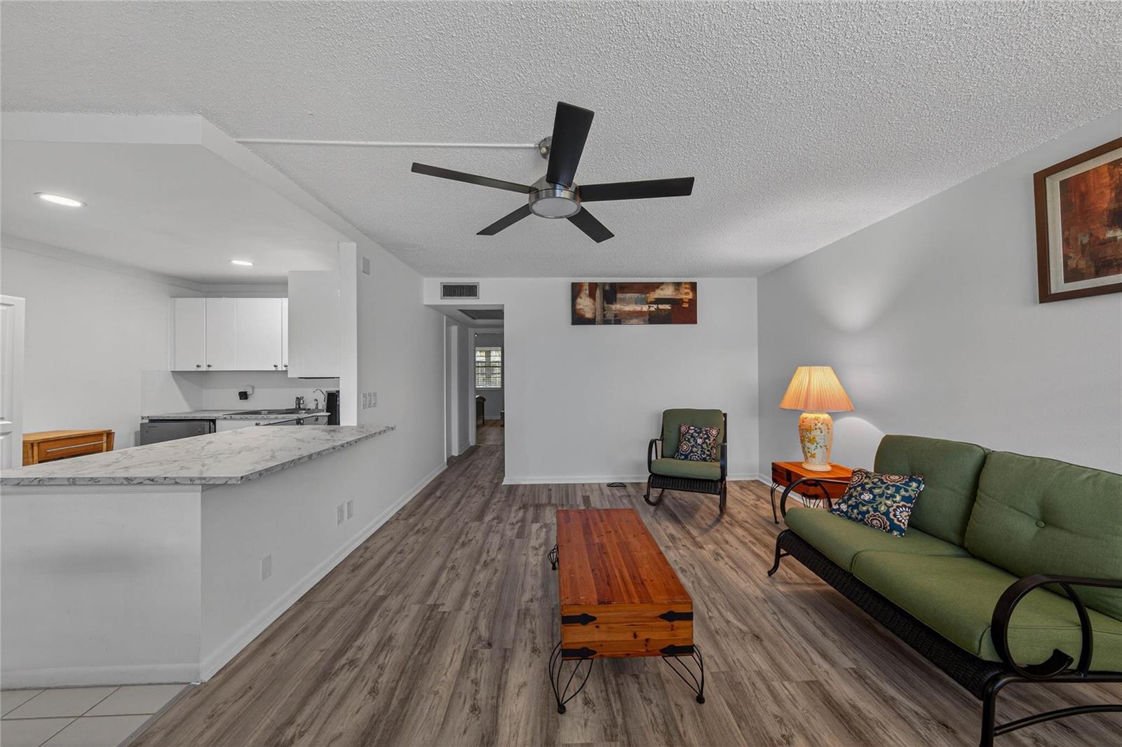 A living room features wood-look flooring, a ceiling fan, and an open kitchen with counters — 51 Farnham C, Deerfield Beach FL 33442, DEERFIELD BEACH, FL