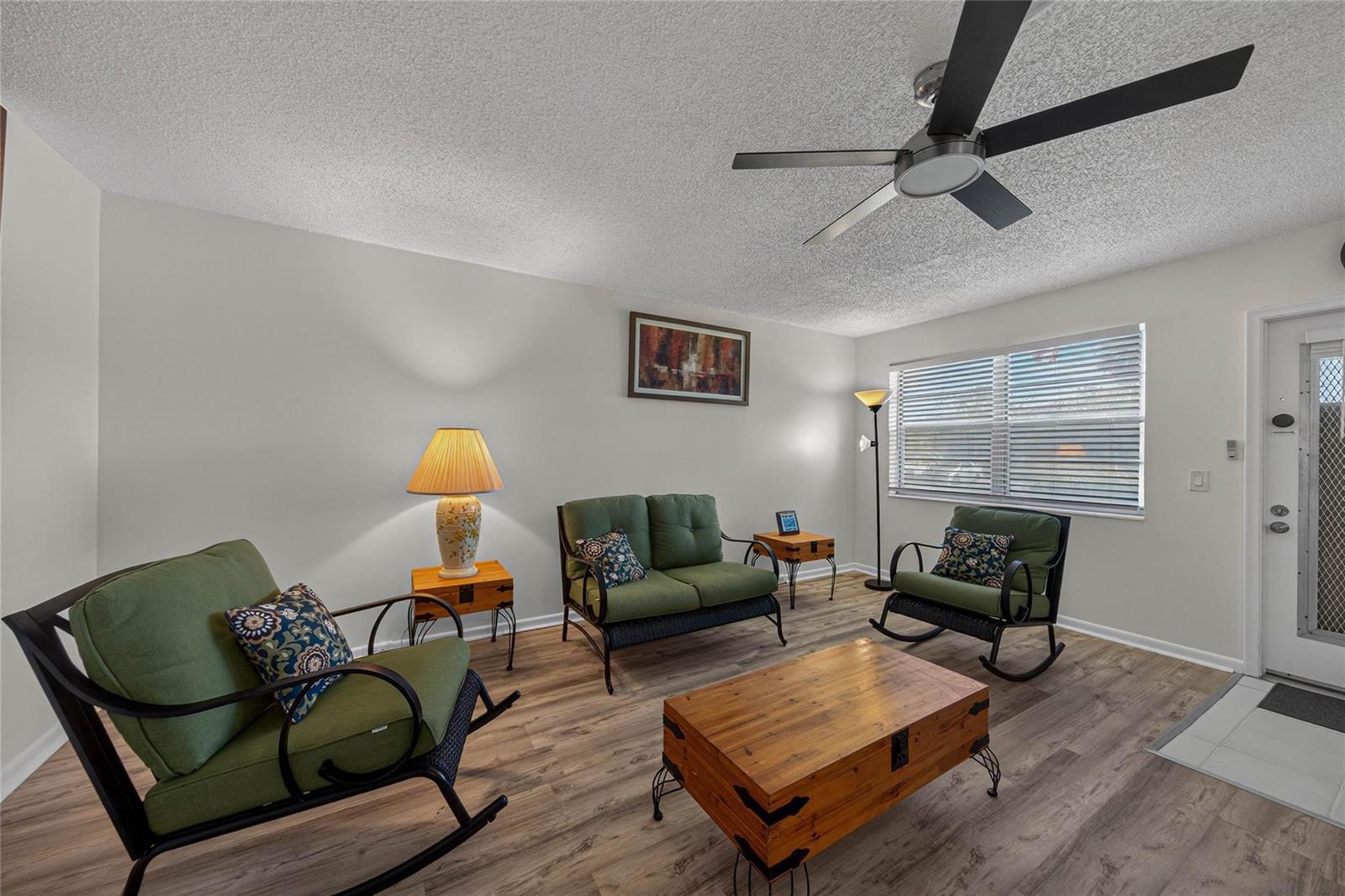 A living room features green rocking chairs, a loveseat, wood-look flooring, and a ceiling fan — 51 Farnham C, Deerfield Beach FL 33442, DEERFIELD BEACH, FL