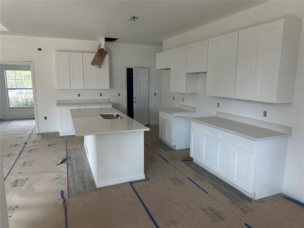 An unfinished kitchen features white cabinets, quartz countertops, a center island, and protective floor covering — 5462 GAGNON TERRACE, NORTH PORT, FL