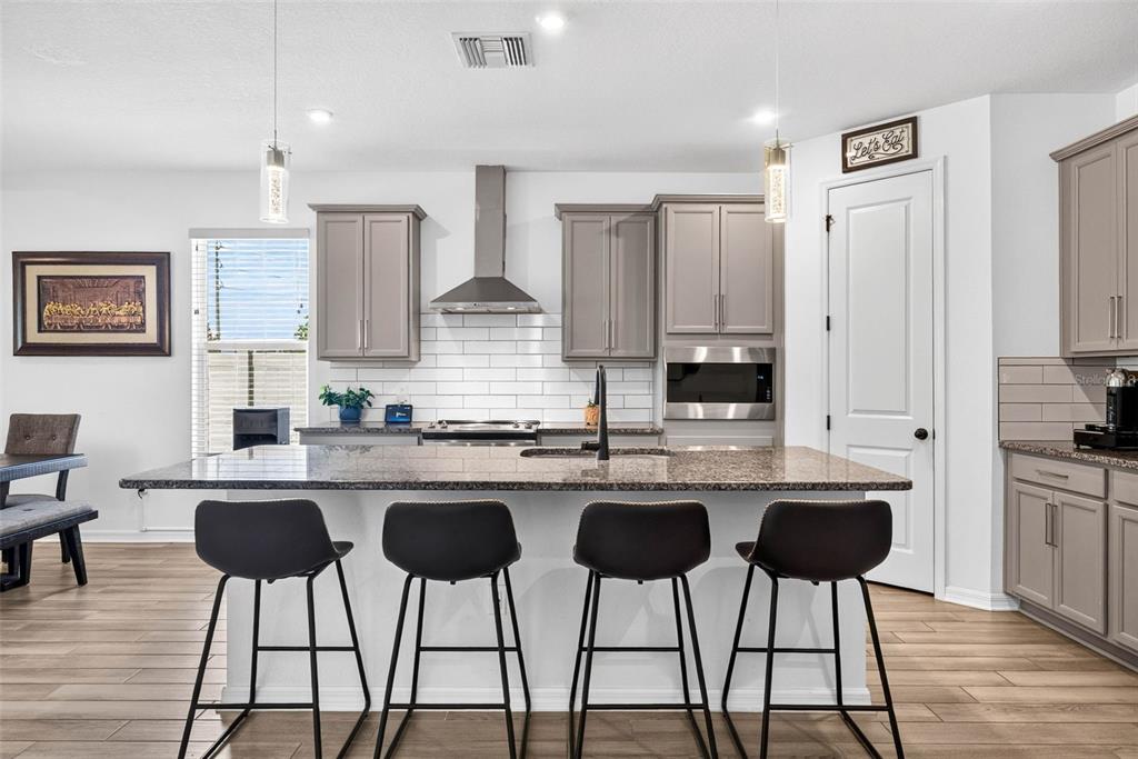 A modern kitchen features gray cabinets, a granite island with four stools, and white backsplash — 13471 NEWPORT SHORES DRIVE, HUDSON, FL