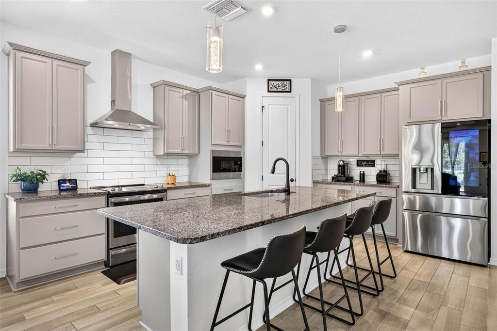 A modern kitchen features light gray cabinets, granite countertops, a central island, and stainless appliances — 13471 NEWPORT SHORES DRIVE, HUDSON, FL