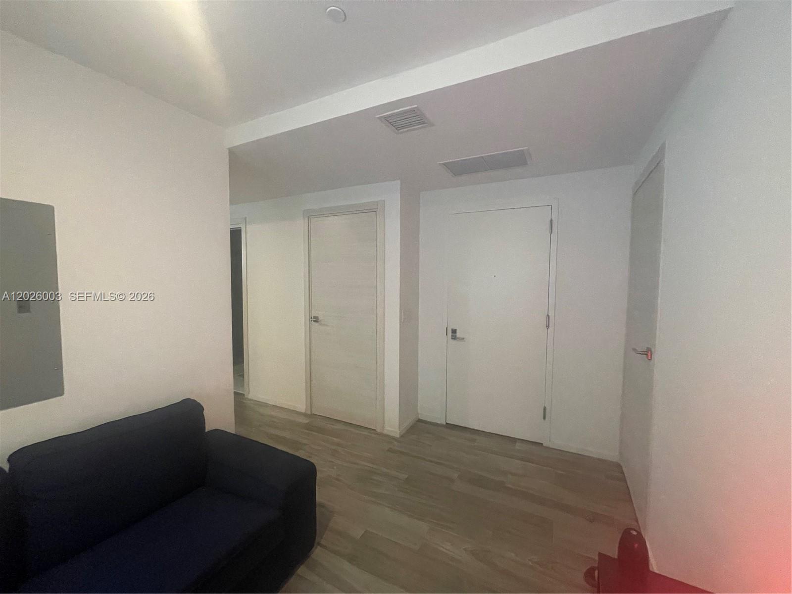 A room with light wood flooring, a dark blue sofa, and three white interior doors — 801 S Miami Ave # 2207, Miami FL 33130, MIAMI, FL