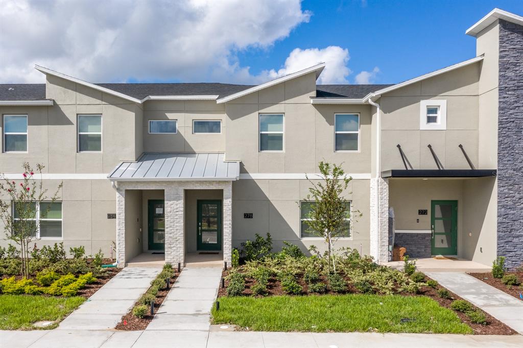 A row of three modern townhomes with beige stucco, stone accents, and green front doors — 278 OCEAN COURSE AVENUE, DAVENPORT, FL
