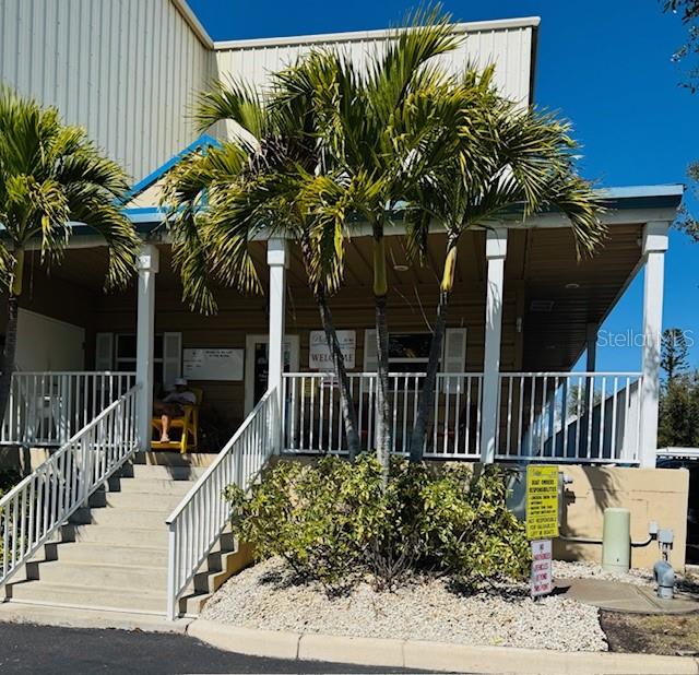 A building exterior features a covered porch with white railings, stairs, and palm trees — 1780 PHILLIPPI SHORES DRIVE UNIT A3-22, SARASOTA, FL