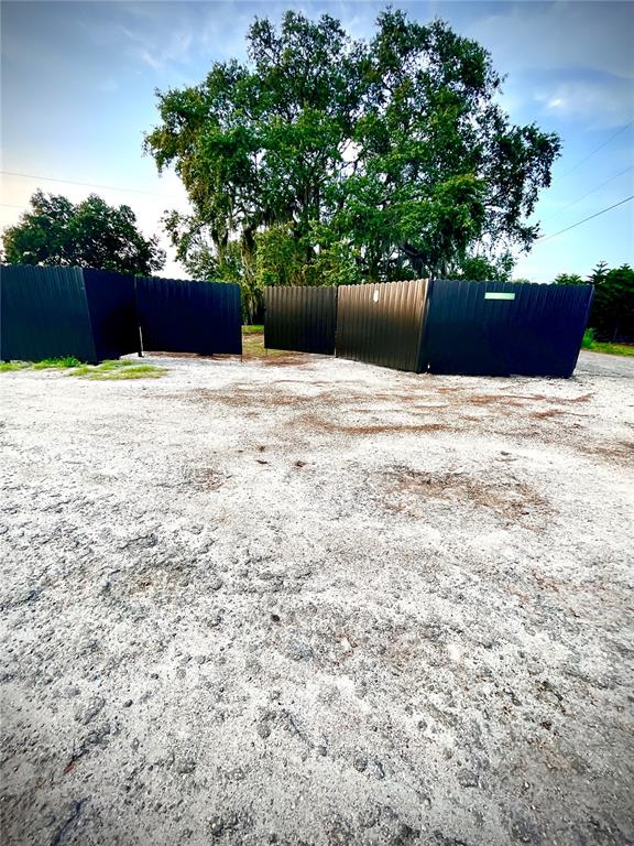 A gravel lot features a dark metal privacy fence in front of a large tree — 6009 MCKINLEY AVENUE, WIMAUMA, FL