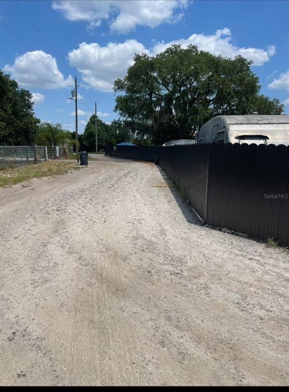 A dirt driveway leads past a black metal fence toward a large tree and trailer — 6009 MCKINLEY AVENUE, WIMAUMA, FL