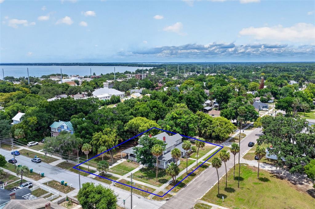 An aerial view shows a two-story house surrounded by trees and streets near water — 527 E LEMON AVENUE, EUSTIS, FL