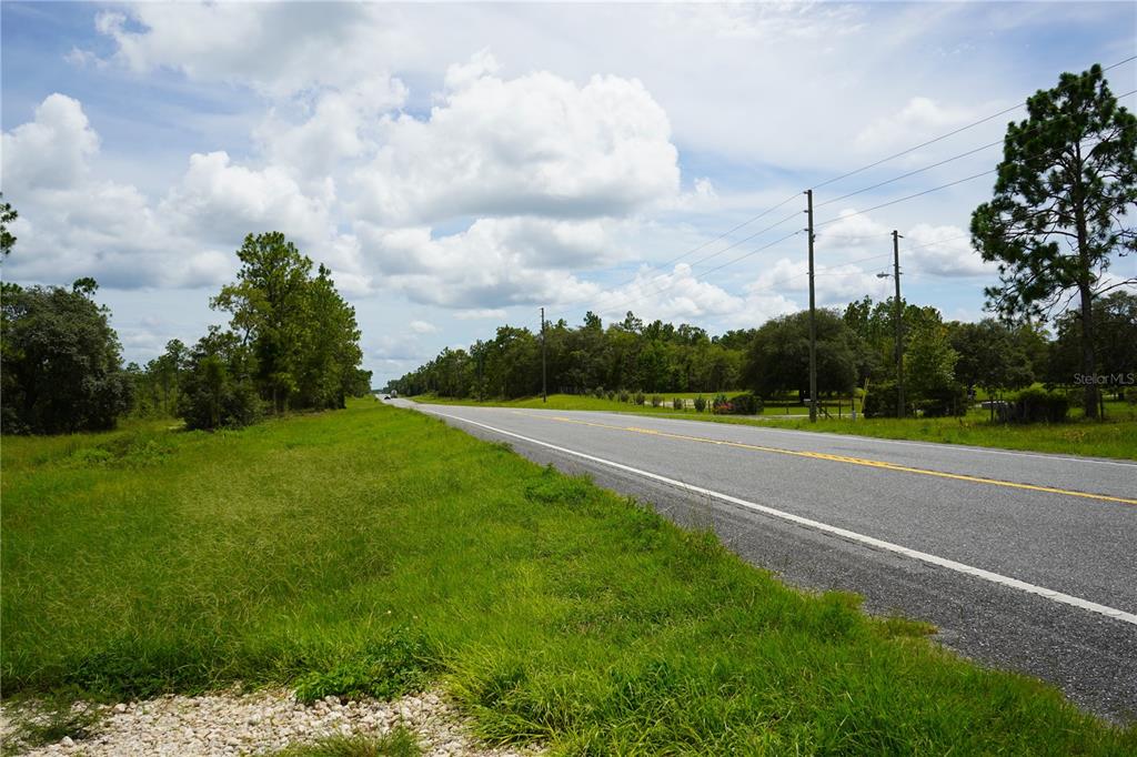 A paved road stretches through a grassy, tree-lined landscape under a cloudy sky — SE STATE ROAD 121 LOT C & D, MORRISTON, FL