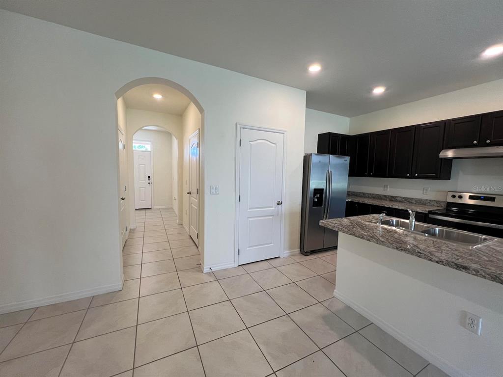 A kitchen with dark cabinets and granite countertops leads into a tiled hallway with arched entryways — 1370 YELLOW FINCH DRIVE, DAVENPORT, FL