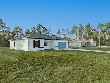 A white, single-story house with a blue garage door sits on a grassy lot — 13195 SW 67TH AVENUE, OCALA, FL