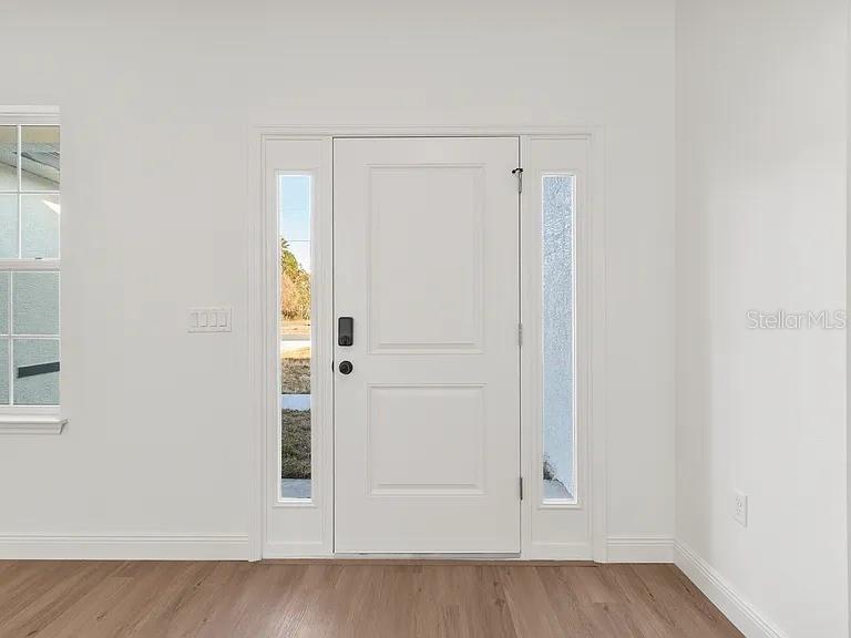 A white front door with sidelights and a nearby window in a room with flooring — 13195 SW 67TH AVENUE, OCALA, FL