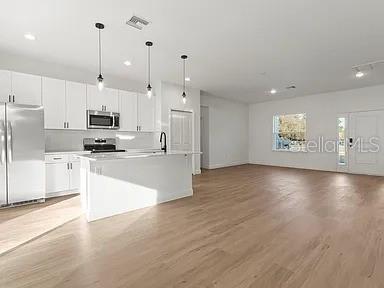 A modern kitchen with white cabinets, stainless steel appliances, and an island features light wood flooring — 13195 SW 67TH AVENUE, OCALA, FL