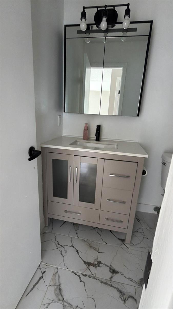 A bathroom vanity with a white countertop, gray cabinets, and a mirror with lighting — 47 SE 13th Street # 2, Dania Beach FL 33004, DANIA BEACH, FL