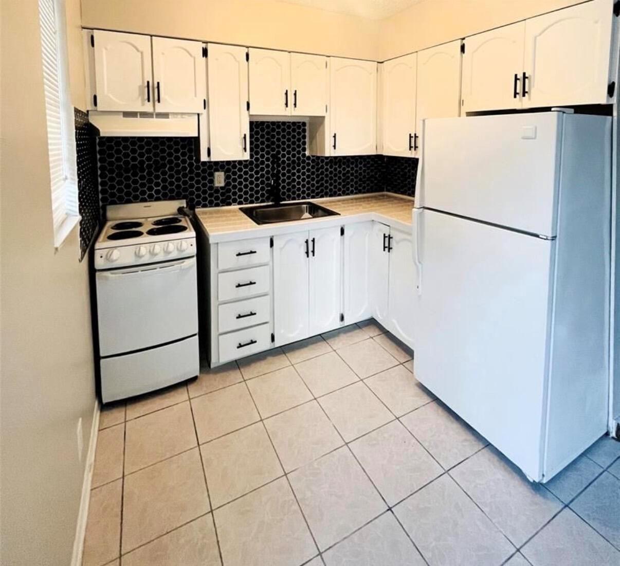 A small kitchen features white cabinets, a white stove, a white refrigerator, and black backsplash — 47 SE 13th Street # 2, Dania Beach FL 33004, DANIA BEACH, FL