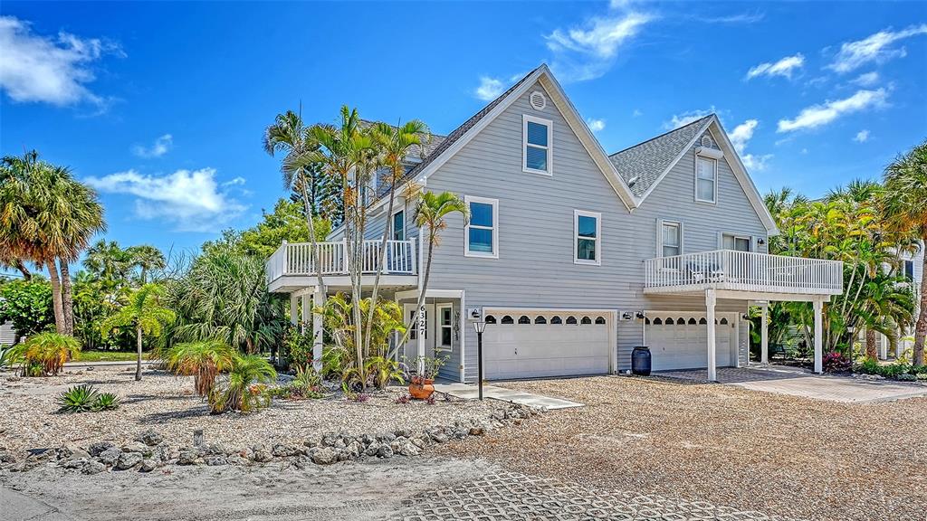 A light blue, two-story coastal house with a gravel driveway and palm trees — 6327 GULF DRIVE, HOLMES BEACH, FL