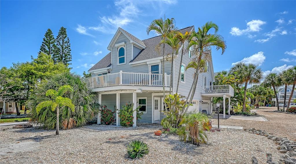 A light gray, two-story coastal house features a wrap-around balcony and palm trees — 6327 GULF DRIVE, HOLMES BEACH, FL