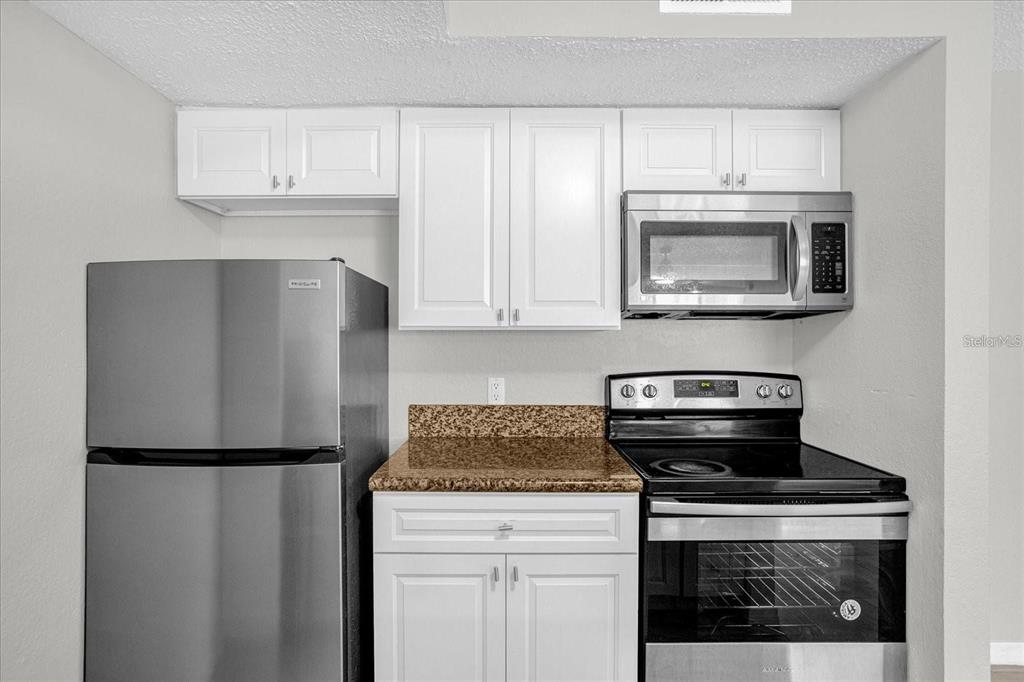 A kitchen features white cabinets, granite countertops, and stainless steel appliances — 5132 CONROY ROAD UNIT 928, ORLANDO, FL