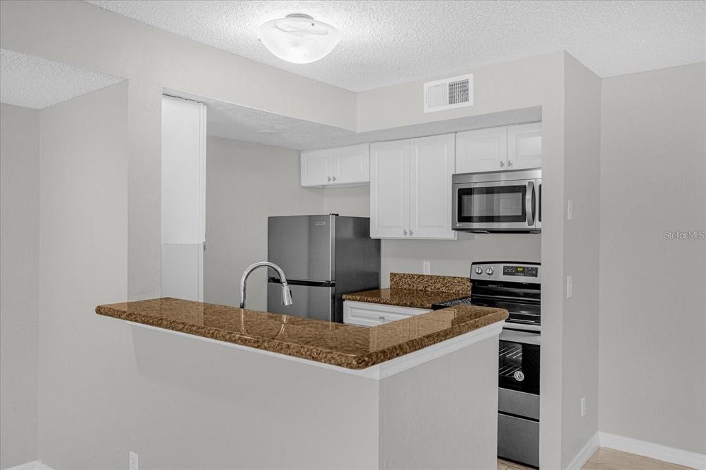 A kitchen features white cabinets, granite countertops, stainless steel appliances, and a breakfast bar — 5132 CONROY ROAD UNIT 928, ORLANDO, FL