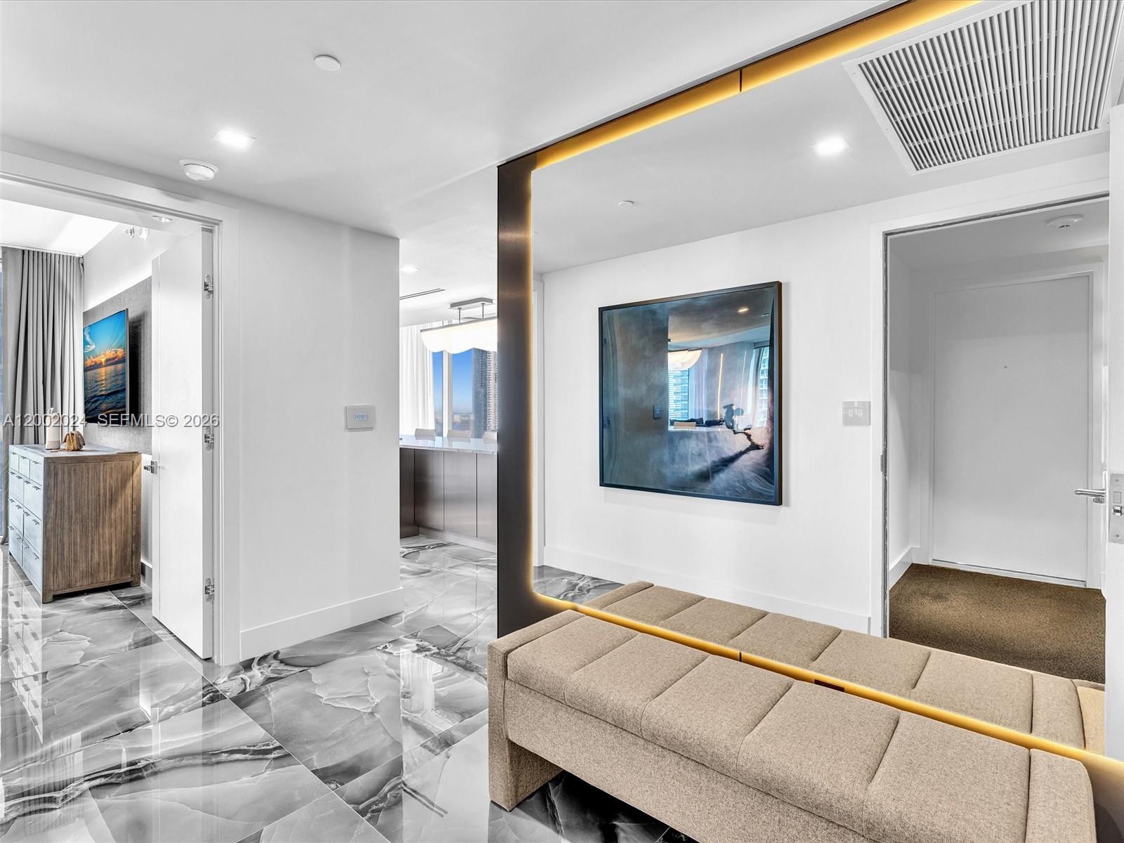 A modern hallway features marble flooring, a large wall mirror, and a beige upholstered bench — 475 Brickell Ave # 2715, Miami FL 33131, MIAMI, FL