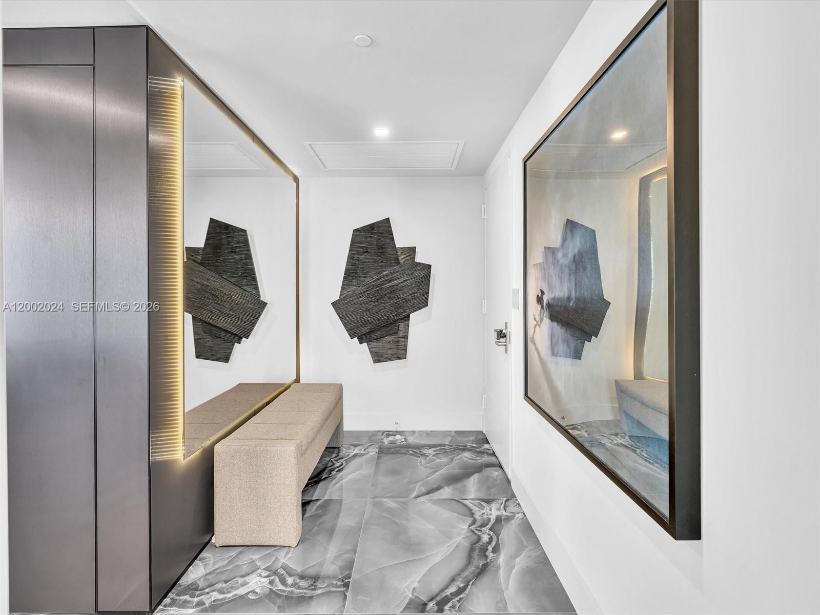 A modern entryway features a bench, large wall mirrors, abstract wall art, and marble flooring — 475 Brickell Ave # 2715, Miami FL 33131, MIAMI, FL