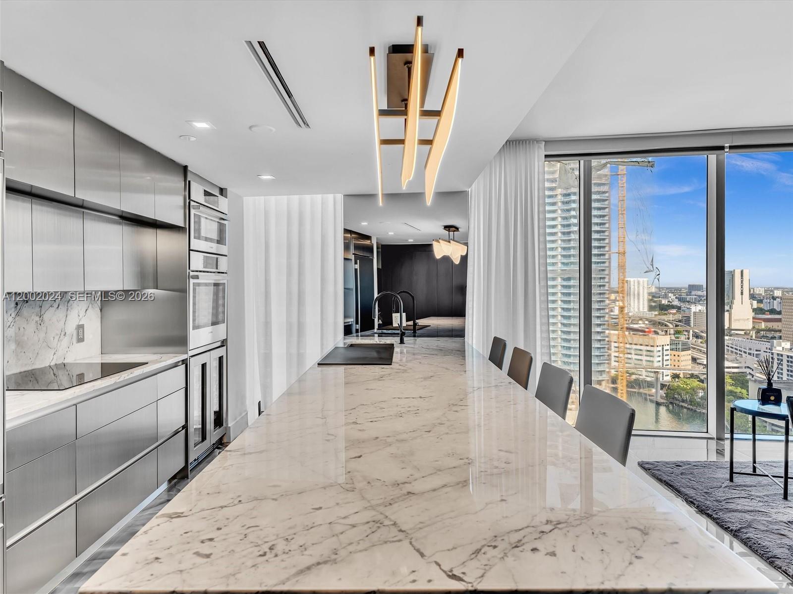 A modern kitchen features a long marble island, stainless steel cabinets, and floor-to-ceiling windows — 475 Brickell Ave # 2715, Miami FL 33131, MIAMI, FL