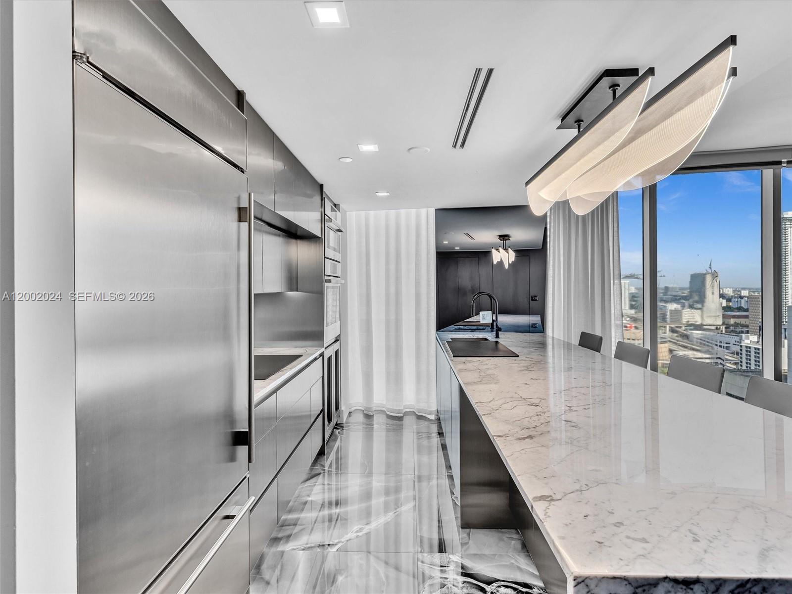 A modern kitchen features stainless steel appliances, a marble island, and floor-to-ceiling city views — 475 Brickell Ave # 2715, Miami FL 33131, MIAMI, FL