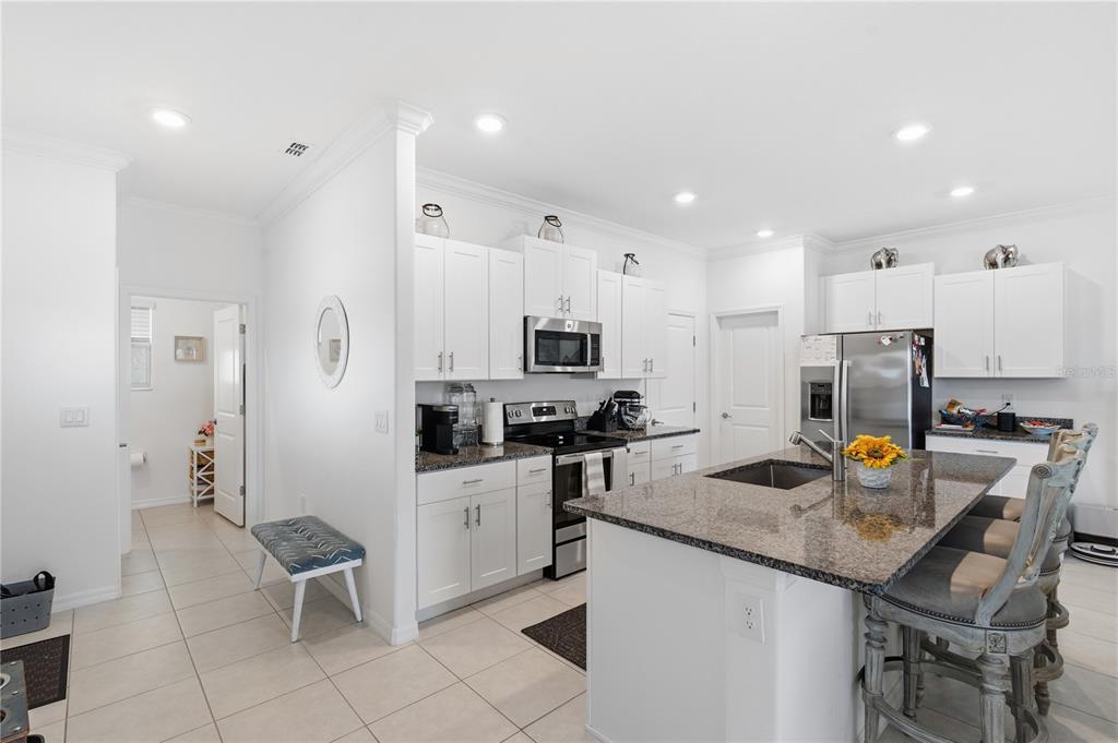 A bright kitchen features white cabinets, granite countertops, a center island, and stainless steel appliances — 9735 ASHWORTH PLACE, LAND O LAKES, FL