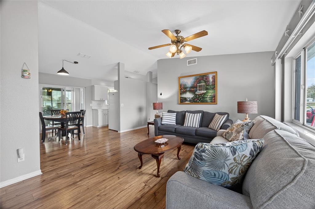 A living room with wood flooring, a grey sofa, and an adjacent dining area — 6196 SW 101ST PLACE, OCALA, FL