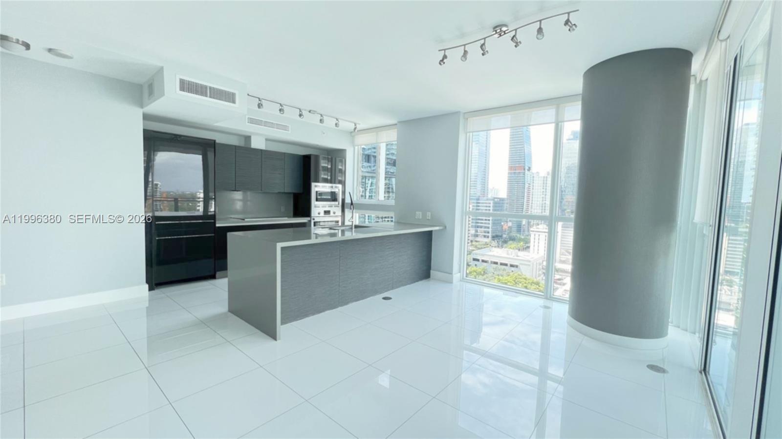 A modern kitchen features dark cabinetry, a gray island, and floor-to-ceiling windows with city views — 1080 Brickell Ave # 1801, Miami FL 33131, MIAMI, FL
