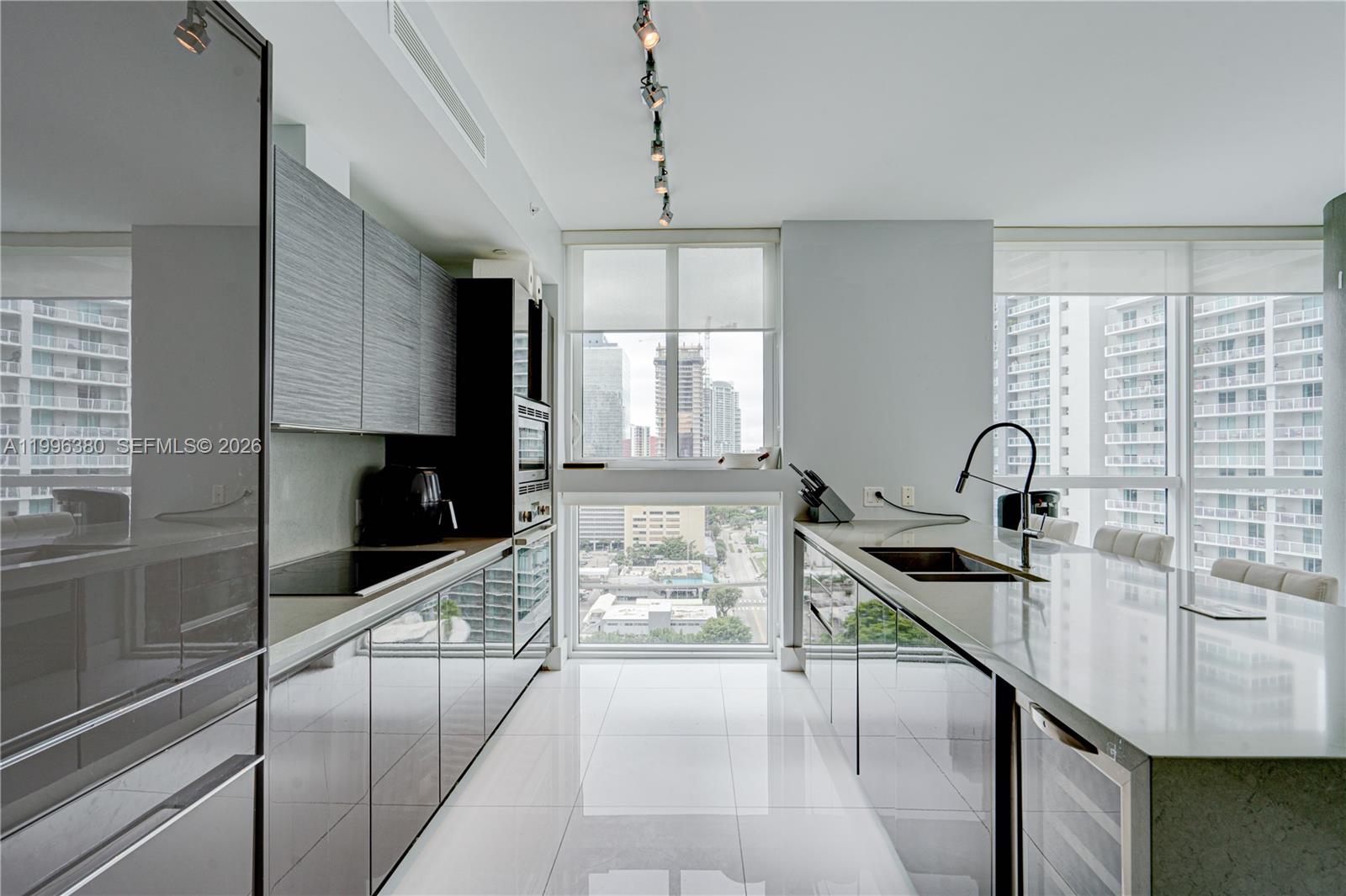 A modern kitchen features glossy gray cabinetry, white tile floors, and floor-to-ceiling city views — 1080 Brickell Ave # 1801, Miami FL 33131, MIAMI, FL